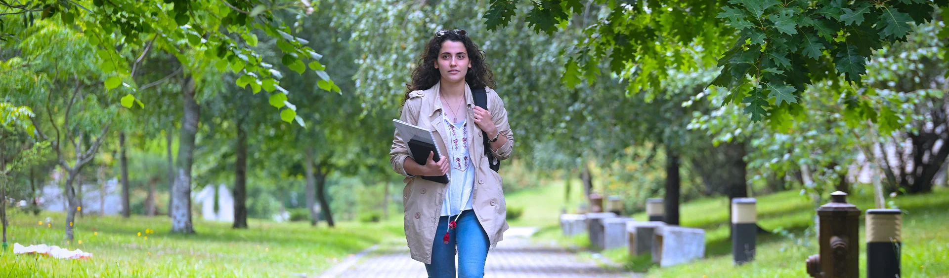 Estudante a caminhar nos jardins do campus da Faculdade de Ciências da Universidade do Porto com livros na mão