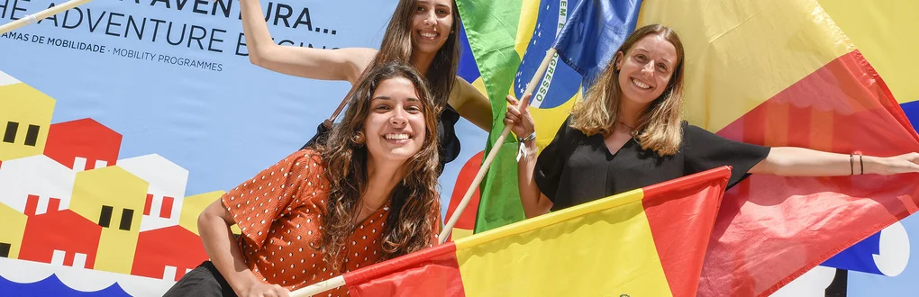 Três estudantes internacionais a segurarem bandeiras dos seus países