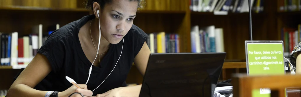 Uma estudante a estudar com o computador numa biblioteca